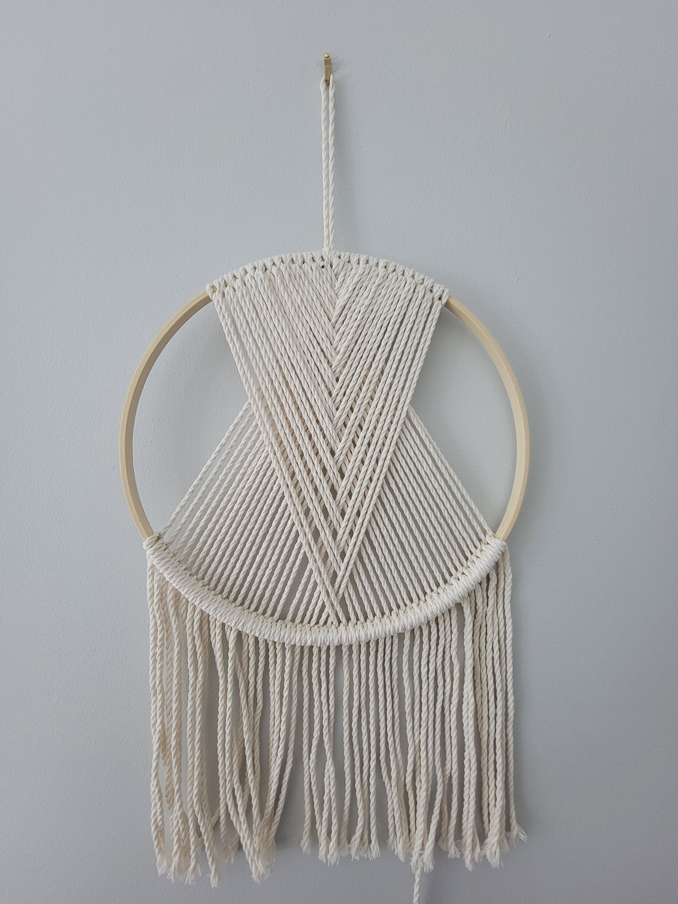 Une décoration murale en macramé avec un cadre en bois, ornée d’un motif géométrique et dotée d’une bordure à franges.