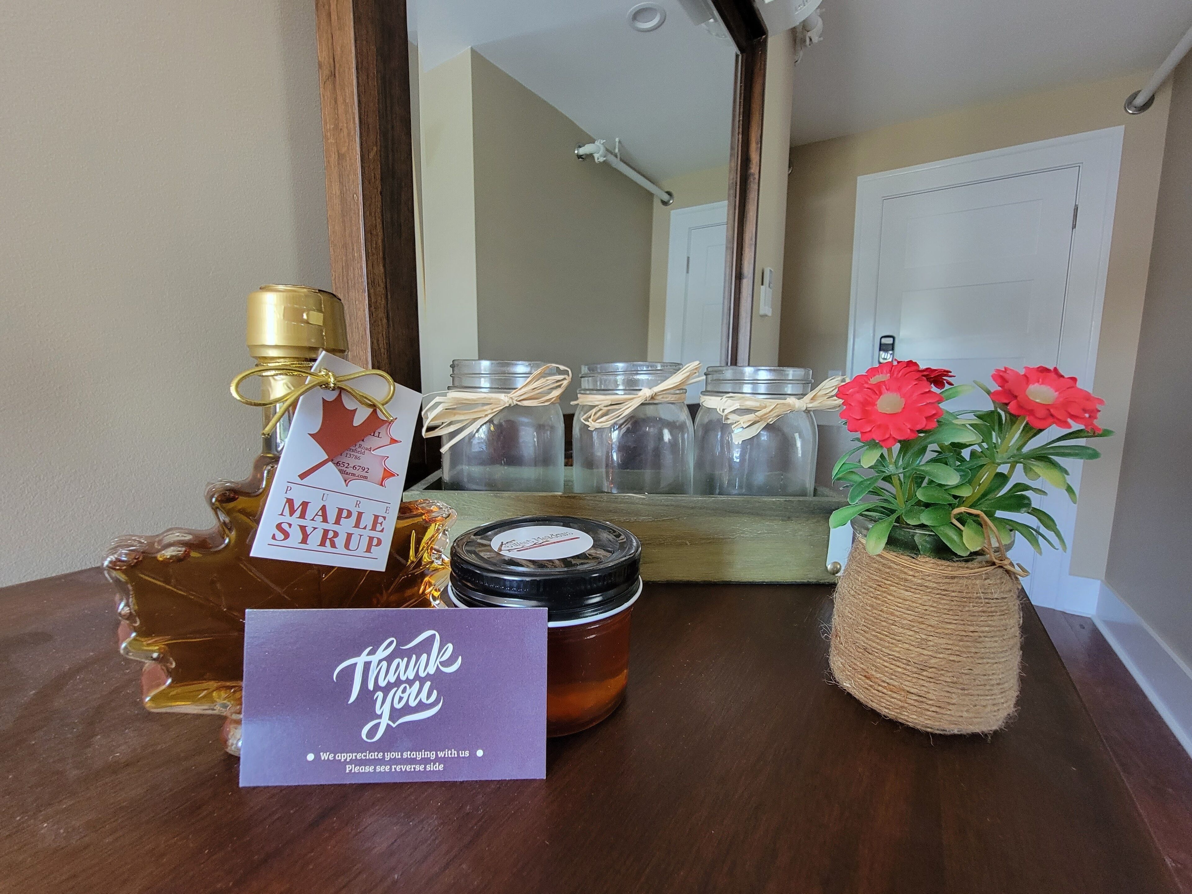 A wooden table with a maple syrup bottle, jars, a thank you card, and a potted plant.