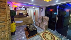 A modern reception area with a wooden reception desk, a large chandelier, and a patterned rug. - OLYMPUS HOTEL & SUITES (Ibadan)