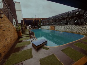 A swimming pool with a brick wall and decorative patterns, surrounded by a patio area with artificial grass and a few lounge chairs.