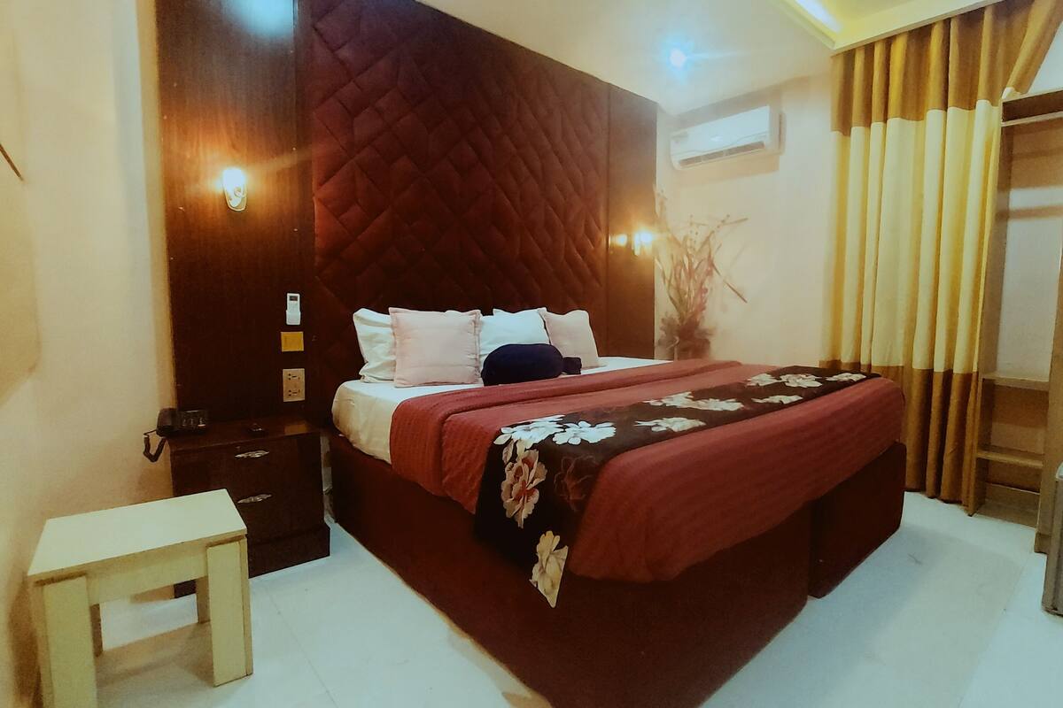 A hotel room with a large bed, a bedside table, a wardrobe, and a kettle on a small table.