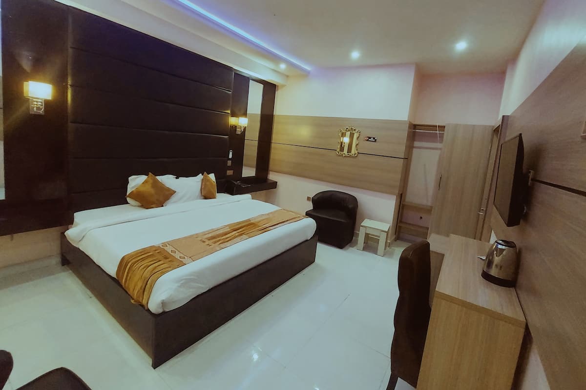 A modern hotel room with a large bed, a desk, a chair, a wardrobe, and a mirror.