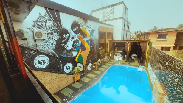A swimming pool with a mural, outdoor seating, and a staircase leading to an upper level. - OLYMPUS HOTEL & SUITES (Ibadan)