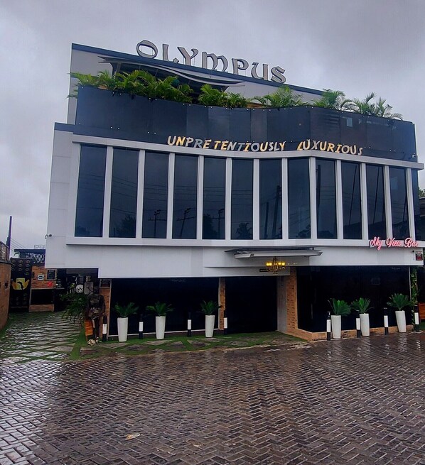 A modern building with the sign "Olympus" and "UNPRETENDENTLY LUXURIOUS" on the facade.