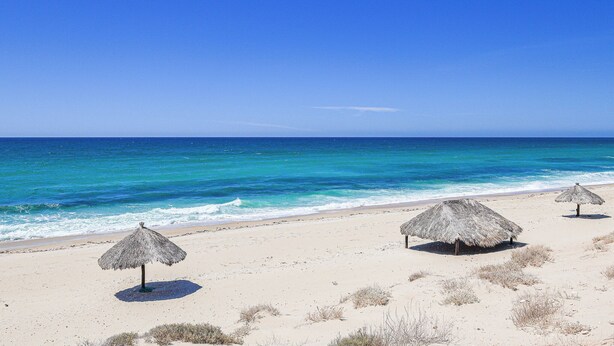 A beach with two thatched umbrellas and a sandy shore.