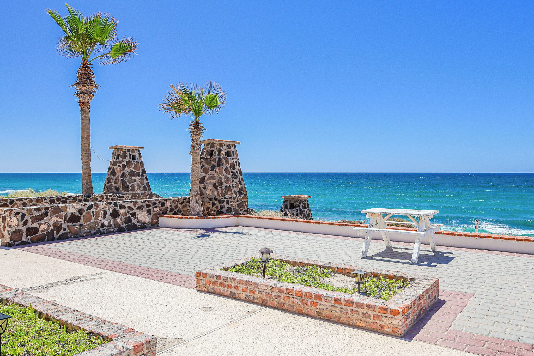 A coastal walkway with stone pillars, a picnic table, and a brick planter.