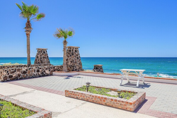 A coastal walkway with stone pillars, a picnic table, and a brick planter.