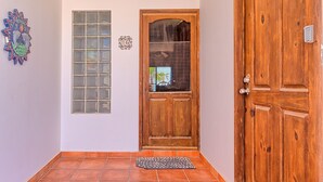 A hallway with a wooden door, a window with a grid pattern, and a decorative wall piece.