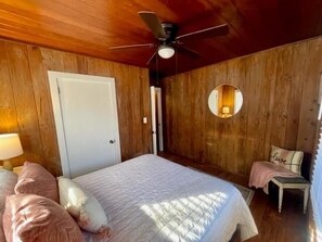 Una habitación con paneles de madera, una cama, un sillón y un ventilador de techo.