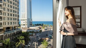 Une femme se tient près d’une fenêtre, d’où l’on peut admirer un paysage urbain comprenant de hauts immeubles et une route où circulent des véhicules.