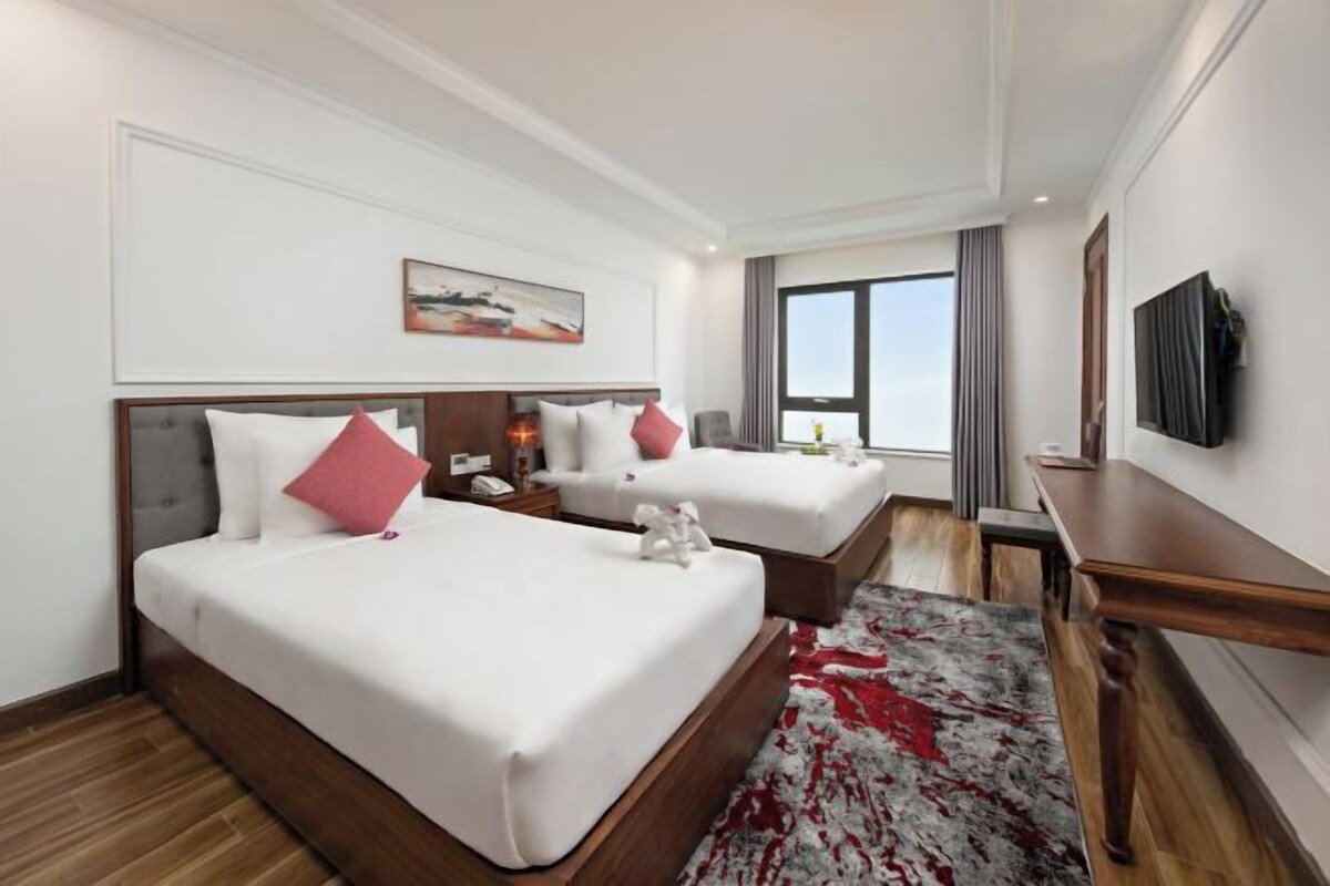 Habitación de hotel con dos camas, piso de madera, un ventanal grande y un televisor de pantalla plana montado en la pared.