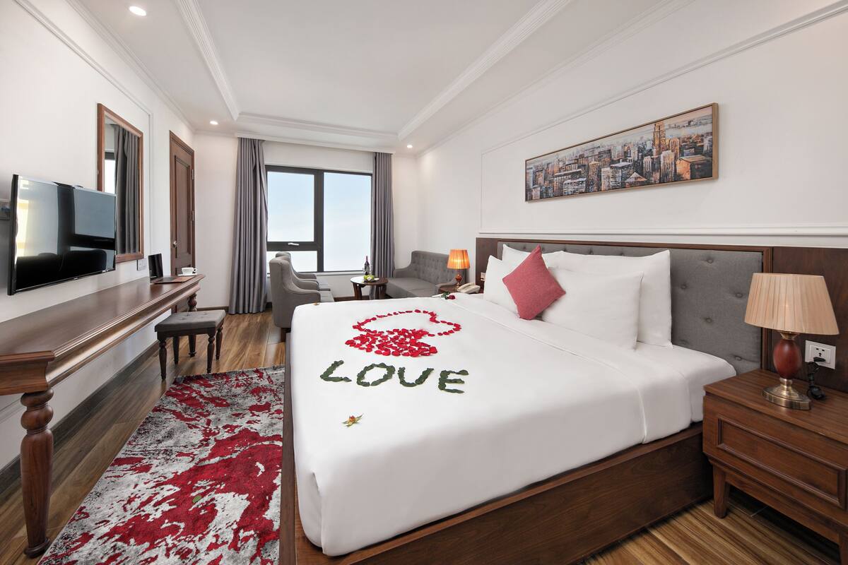 Ein Hotelzimmer mit Bett, Schreibtisch, Fernseher und einem Stadtbild an der Wand.