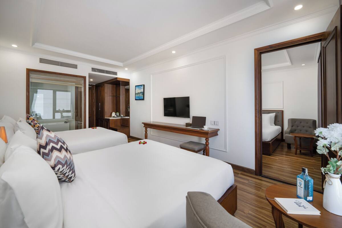 Ein Hotelzimmer mit zwei Betten, einem Schreibtisch mit einem Laptop, einem Fernseher und einer Sitzecke mit Sessel und Tisch.