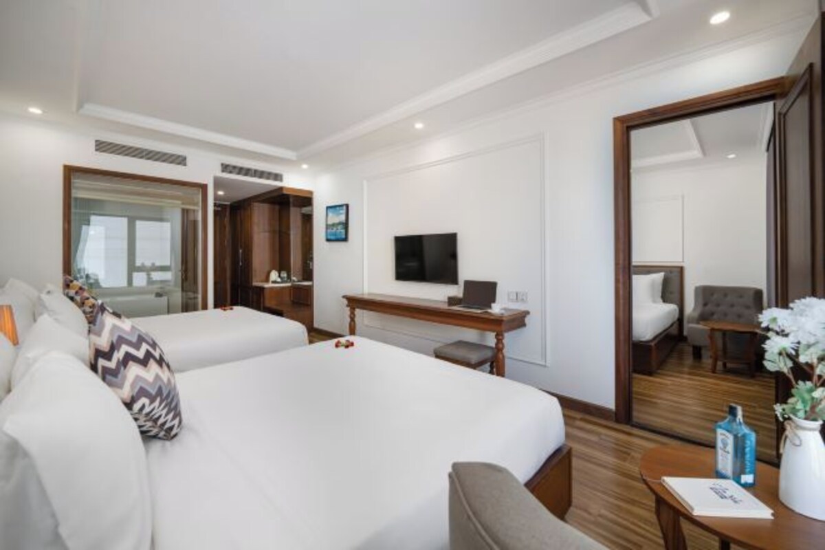 A hotel room with two beds, a desk with a laptop, a TV, and a mirror.