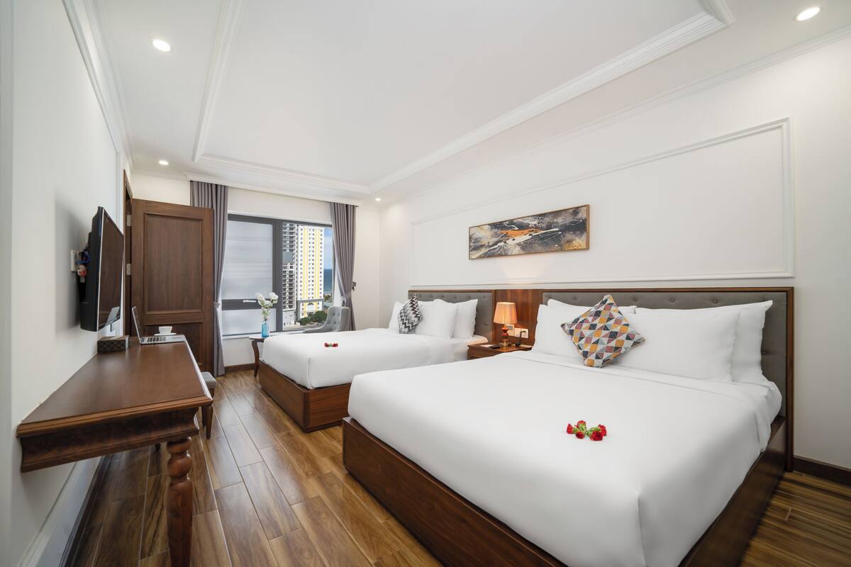 Ein Hotelzimmer mit zwei Betten, einem Holztisch, einem Fernseher und einem Fenster mit Vorhängen.