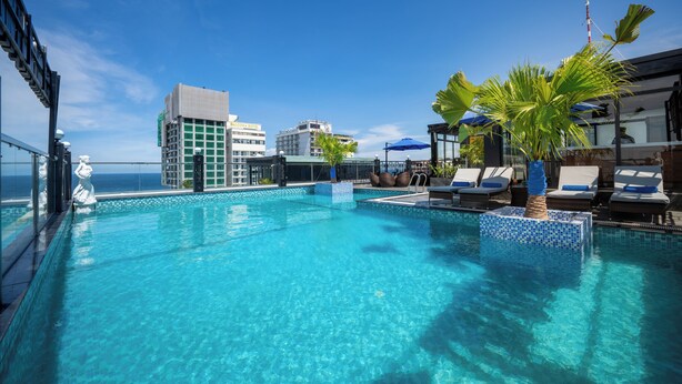 Une piscine sur le toit, avec une eau d’un bleu cristallin, des chaises longues et une vue sur l’océan et les bâtiments.