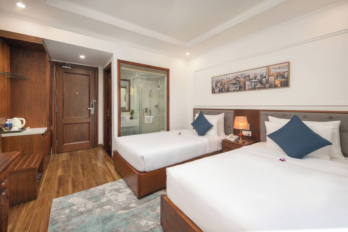 Ein Hotelzimmer mit zwei Betten, einem Holzschrank, einem Badezimmer mit Duschkabine und einem Stadtbild an der Wand.