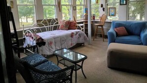 A room with a bed, a blue sofa, a small table, and a chair. There are large windows with views of trees. - Shawnee Forest In Town Retreat (Harrisburg)