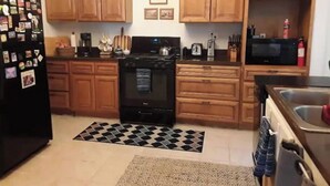 A compact kitchen with wooden cabinets, a black refrigerator, a stove, and a microwave. - Shawnee Forest In Town Retreat (Harrisburg)