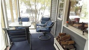 A covered porch with a table and two chairs, a stack of firewood, and a window with a view of the outside. - Shawnee Forest In Town Retreat (Harrisburg)