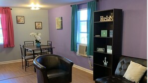 A living room with a black leather sofa, a black coffee table, a dining table with chairs, and a bookshelf labeled "Relax".