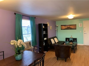 A living room with a sofa, a dining table with chairs, a bookshelf, and a painting on the wall. - 1 BR in the heart of FMB- unit 3 (Fort Myers Beach)