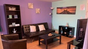A living room with a black leather sofa, a coffee table, a bookshelf, and a painting on the wall.
