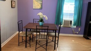 A dining area with a table and chairs, a vase with flowers, a window with curtains, and artwork on the wall.