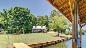 A wooden deck extending over a body of water, with a house and trees in the background. - Amazing rustic cabin with 450' of water frontage on Jackson Lake (Monticello)