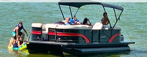 Een boot met een afdak, verschillende mensen aan boord en iemand in een gele luchtbed in het water.