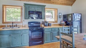 A kitchen with wooden ceiling beams, green cabinets, a black stove, and a refrigerator. - Amazing rustic cabin with 450' of water frontage on Jackson Lake (Monticello)