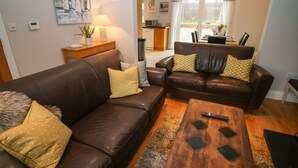 A living room with two brown leather sofas, a wooden coffee table, and a small side table with a lamp. - Pebble Lodge (Kenmare)