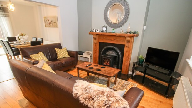 A living room with a brown leather sofa, a wooden coffee table, a fireplace, and a television. - Pebble Lodge (Kenmare)