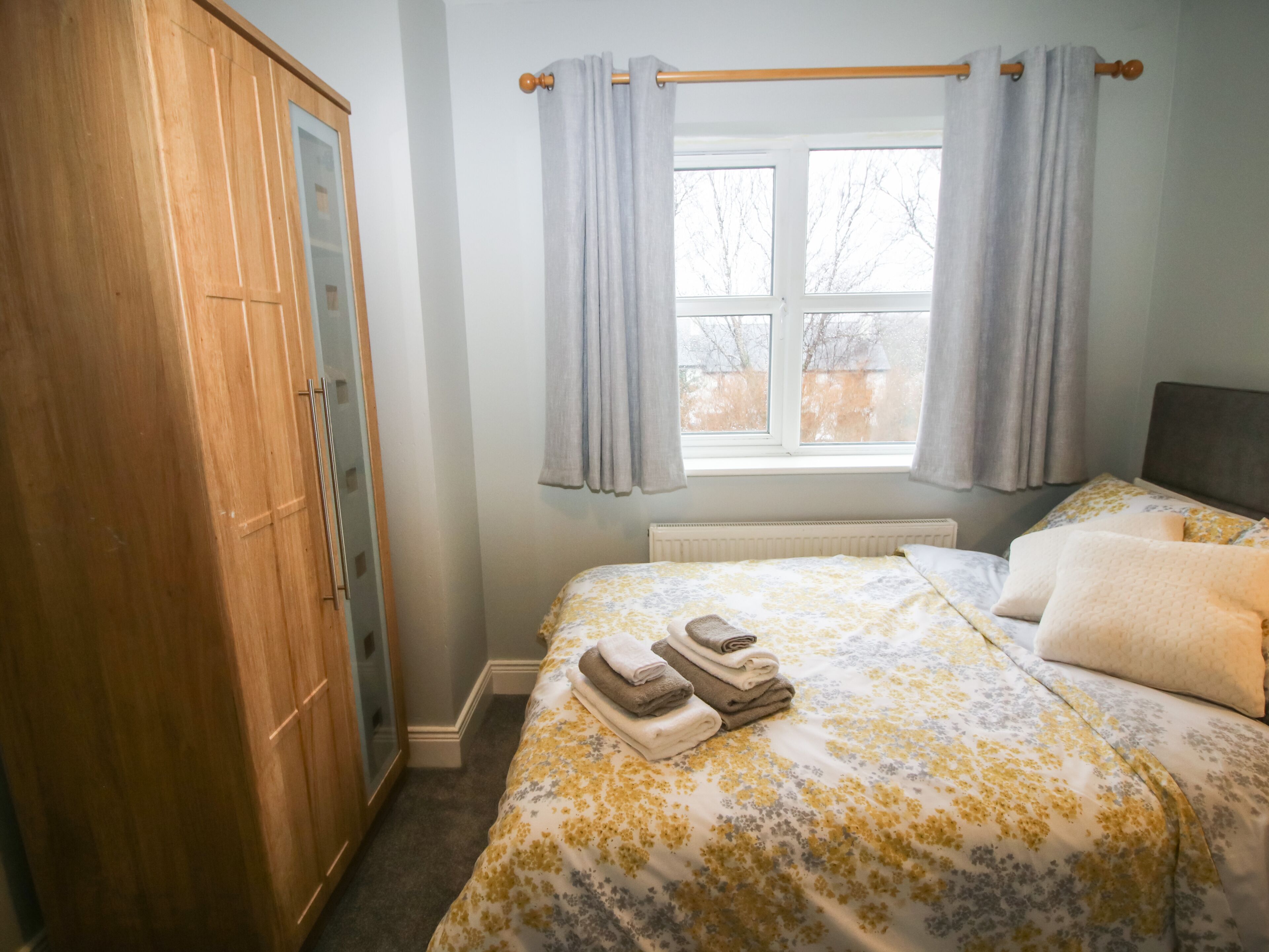 A bedroom with a bed, a wardrobe, a window with curtains, and a radiator.
