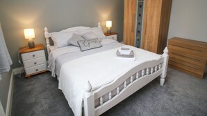 A neatly arranged bedroom with a bed, bedside tables, a wardrobe, and a chandelier. - Pebble Lodge (Kenmare)