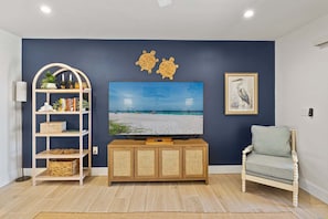 A living room with a flat-screen TV on a wooden cabinet, a bookshelf, a decorative wall piece, and a framed picture.