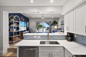 A modern kitchen with a central island, built-in shelving, and a view to an outdoor seating area.