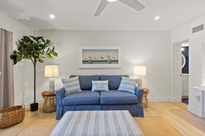 A living room with a sofa, two side tables with lamps, a coffee table, a potted plant, and a framed picture on the wall.