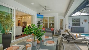 A modern dining area with a glass table, potted plants, and a view of the kitchen and living spaces.