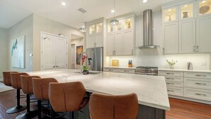 A modern kitchen with white cabinetry, a large island with bar stools, stainless steel appliances, and pendant lighting.