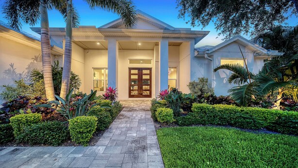 A modern house with a central entrance, a covered porch, and a well-maintained garden with various plants and a lawn.