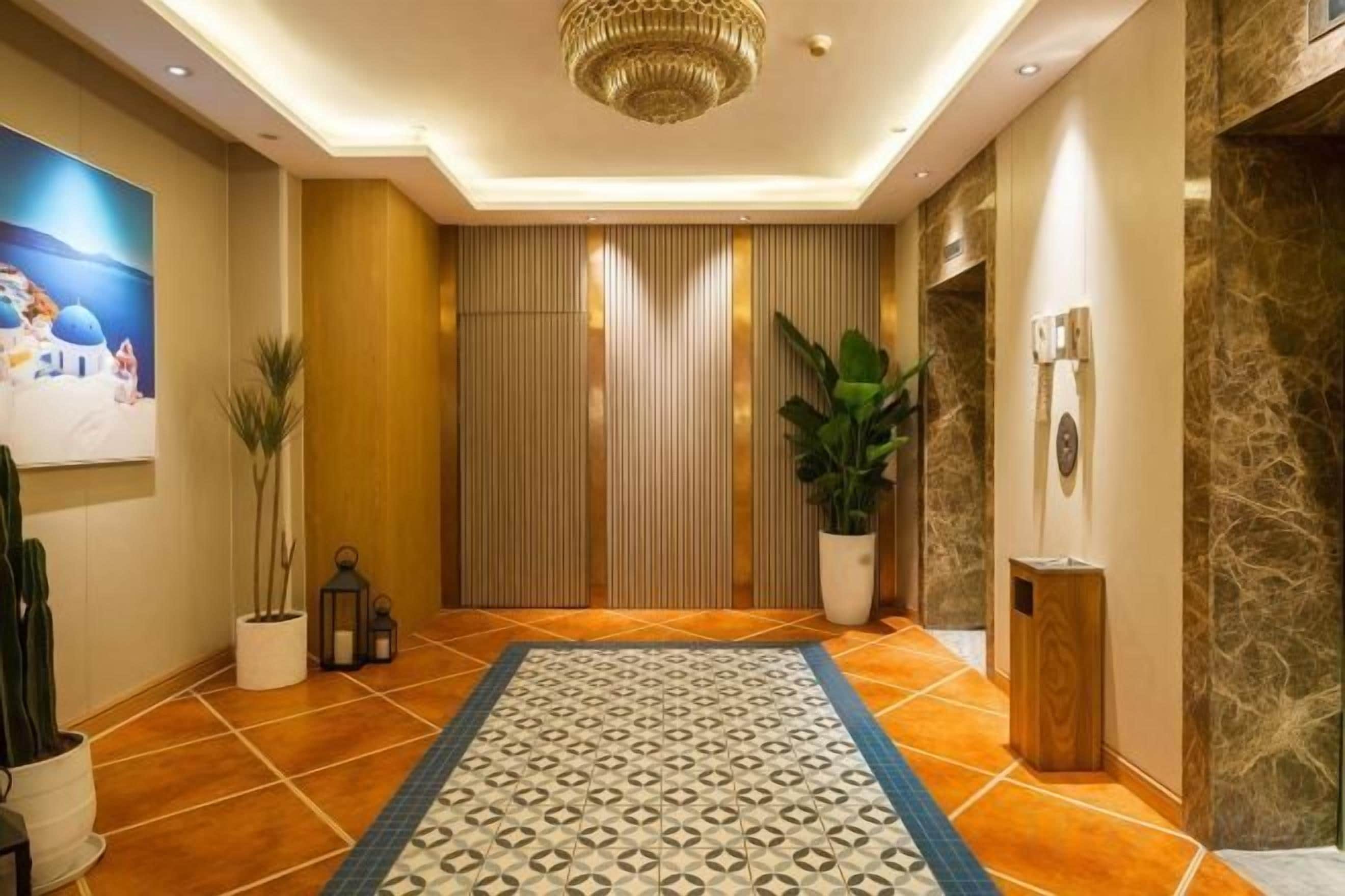 Un hall d’hôtel agrémenté d’un tapis à motifs, de plantes en pot, d’un tableau et d’un lustre moderne.