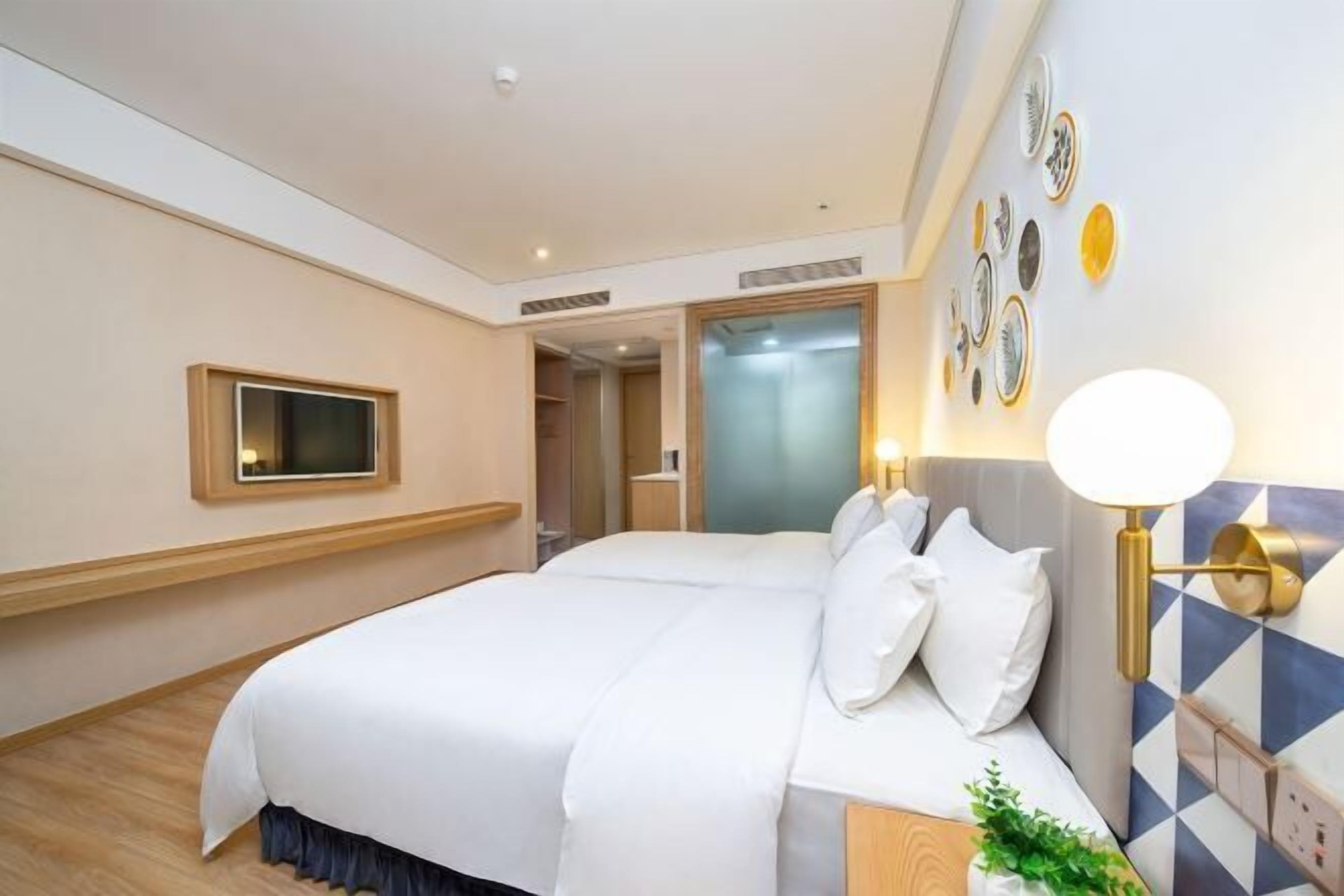 A hotel room with a large bed, a bedside table, a wall-mounted TV, and a wall-mounted lamp.
