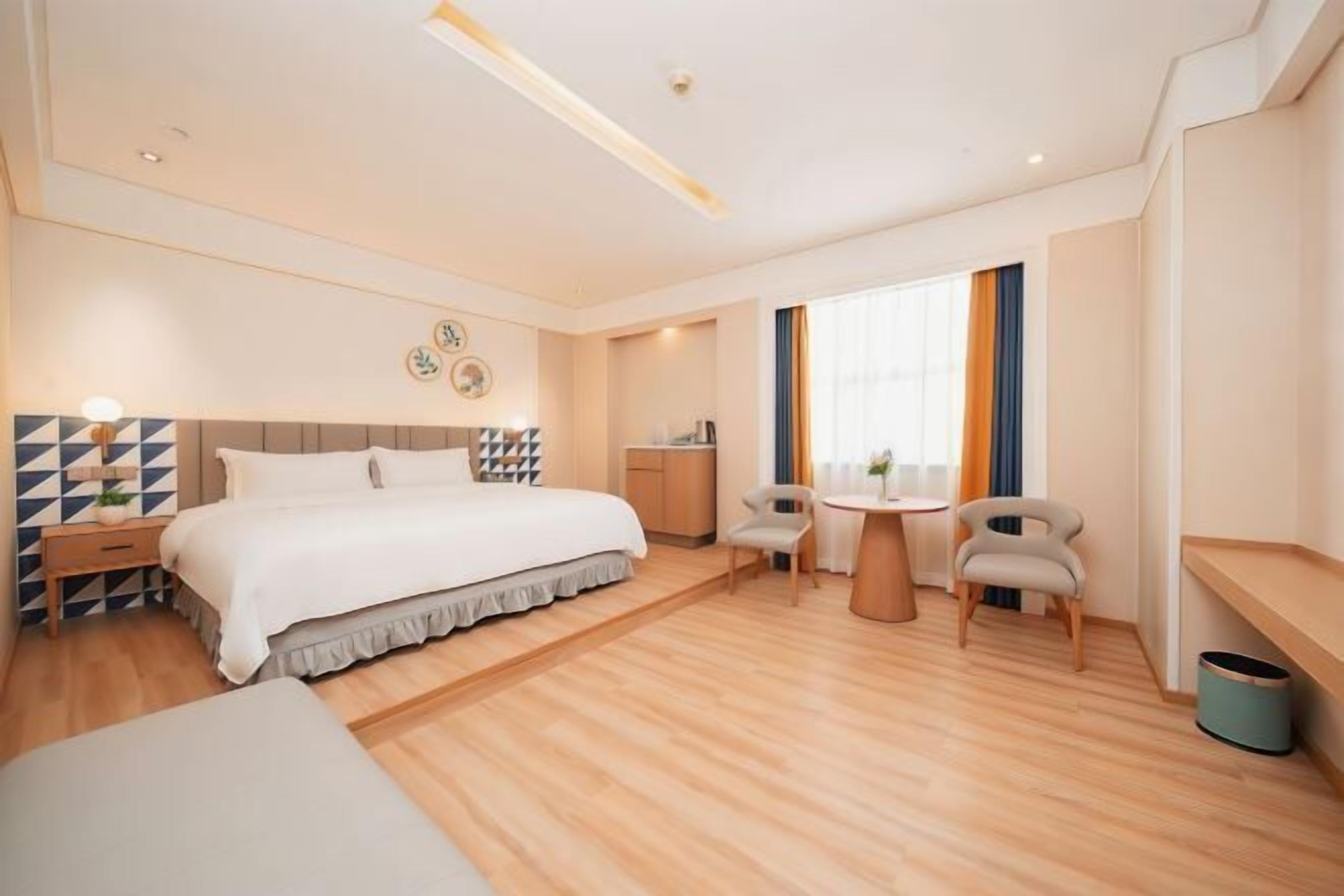 Una habitación de hotel moderna con una cama grande, un escritorio, dos sillas, una mesita y una ventana con cortinas.