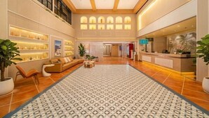 Um hall amplo com um tapete estampado, um balcão de recepção e prateleiras com objetos decorativos.