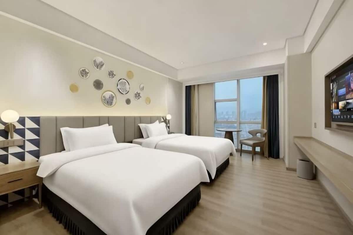 A hotel room with two beds, a desk, a chair, a TV, and a city view.