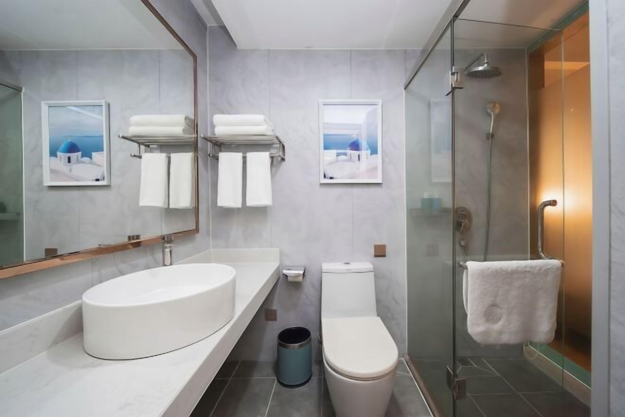 Un baño moderno con un espejo grande, un lavamanos blanco, un inodoro y una ducha con mampara de vidrio.