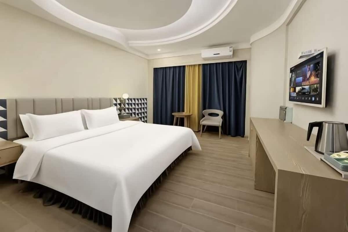 A hotel room with a bed, a desk, a chair, a TV, and a coffee maker.