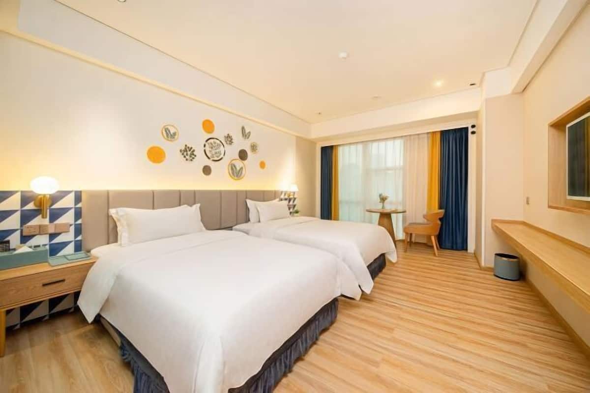 A hotel room with two beds, a small table, a chair, and a decorative wall.