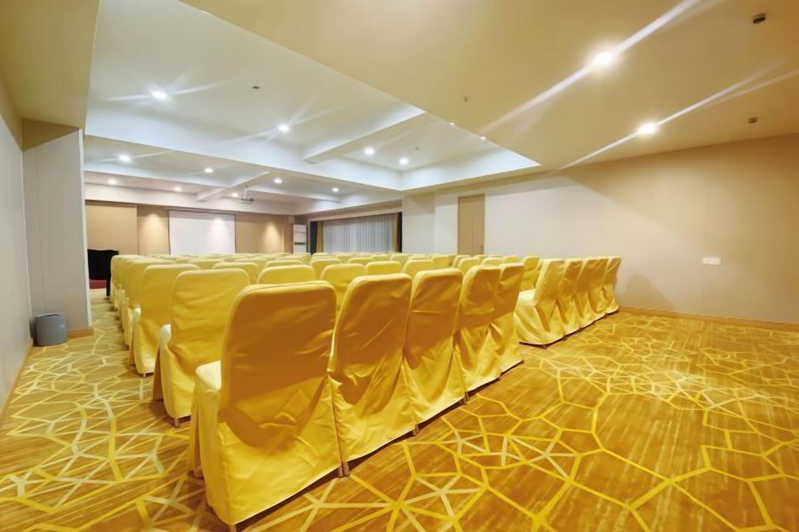 A conference room with rows of yellow chairs, a patterned carpet, and a ceiling with recessed lighting.